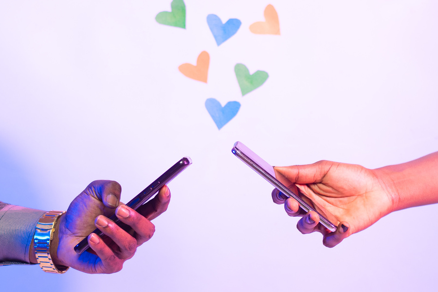 two people using their phones in close proximity to each other, with love shapes above the phones, online dating concept