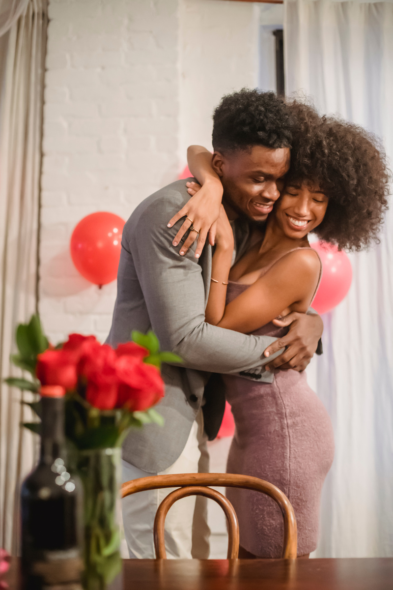 Happy black couple hugging in loft near table with flowers